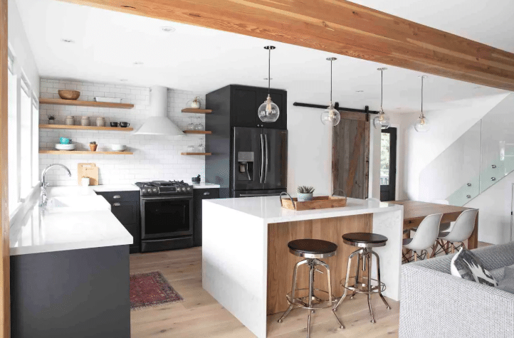 Modern kitchen features black and white cabinetry, a central island with two stools, pendant lights, and a dining area with white chairs—perfect for hosting in one of the luxury Airbnb's in Whistler.