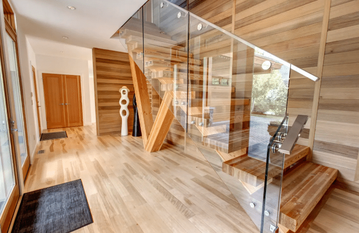 Modern hallway with light wood floors and walls, a glass-paneled staircase, and two white abstract sculptures near double wooden doors—perfect inspiration for luxury airbnb's in Whistler.