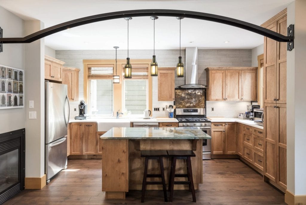 Modern kitchen with wooden cabinets, stainless steel appliances, a central island with a marble top, and three pendant lights overhead—perfectly designed for comfort and security with the best Airbnb cameras discreetly installed.