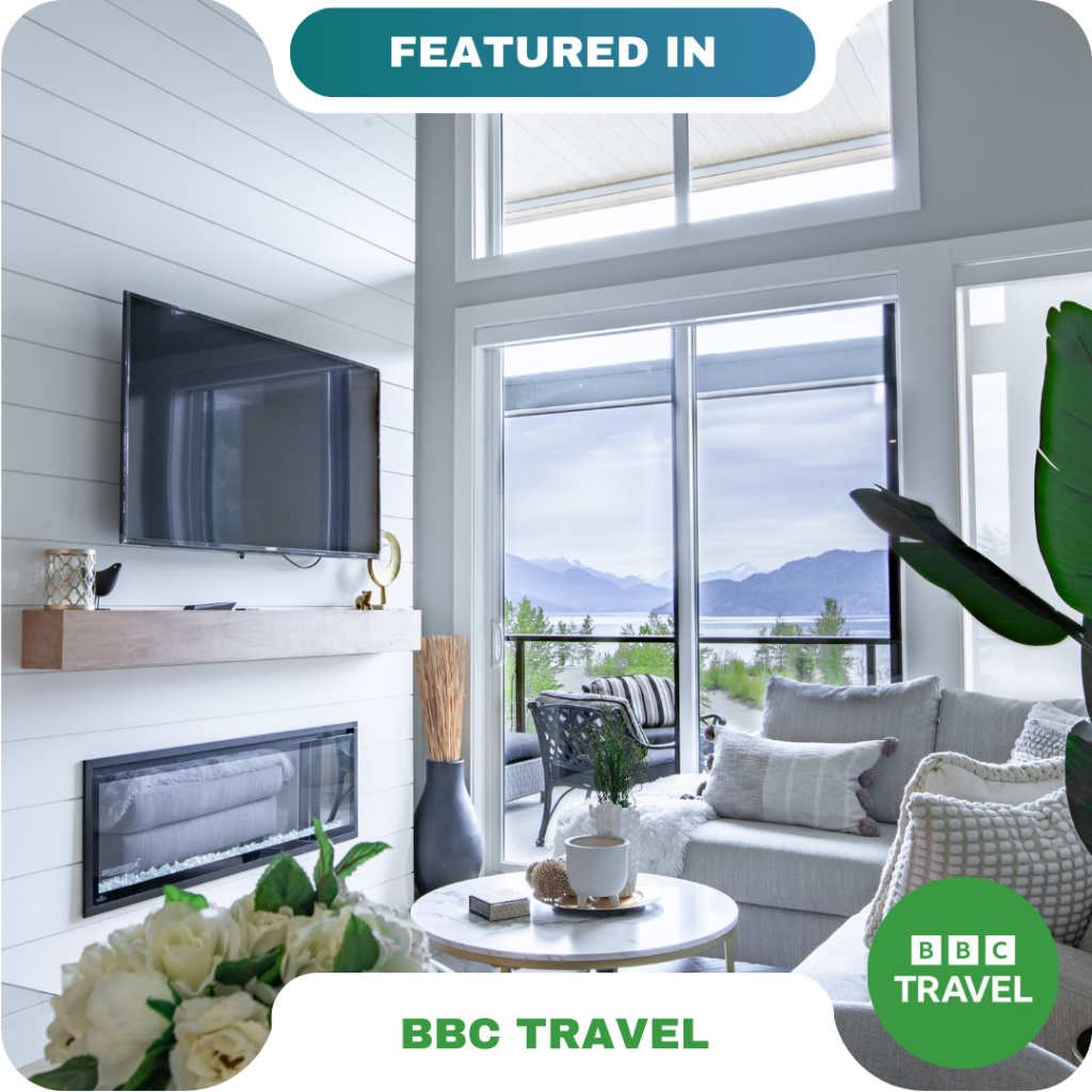 Modern living room with large windows, a wall-mounted TV, fireplace, and neutral decor overlooking a scenic outdoor view—featured in BBC Travel and ideal for relaxing with partners.
