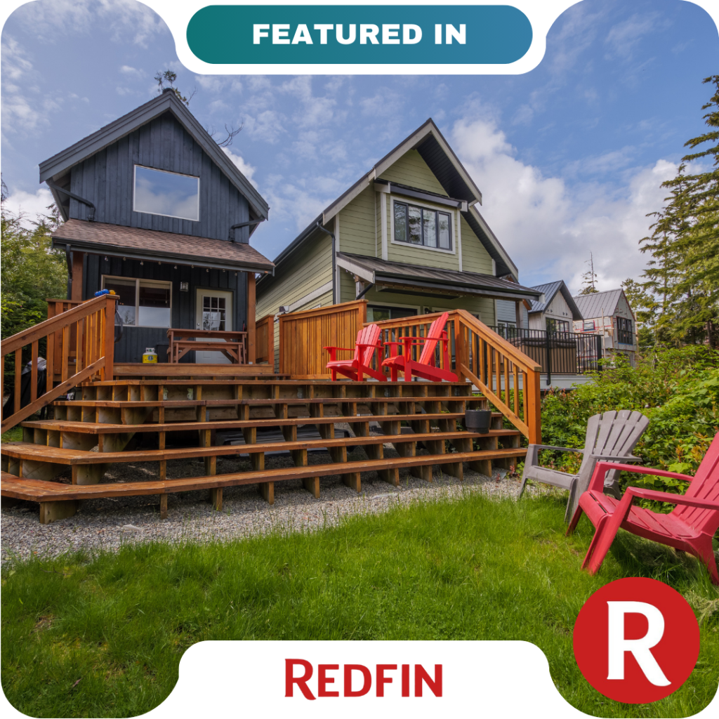 A two-story house with wooden steps and a deck featuring red chairs, surrounded by greenery, under a partly cloudy sky. Redfin branding is visible, highlighting trusted partners in finding your dream home.