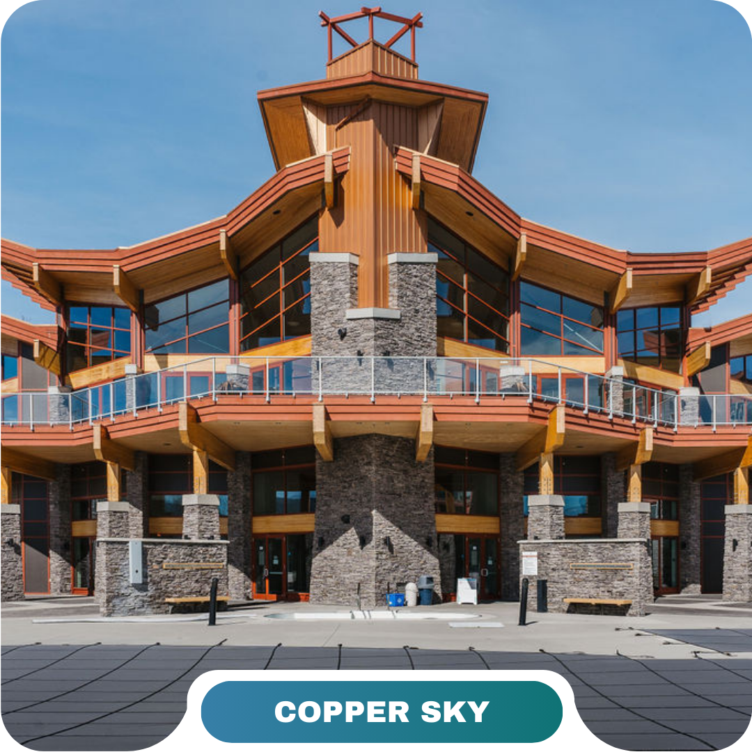 A modern building with wood and stone exterior, large windows, and angular roof features, labeled "Copper Sky" at the bottom—perfect for those seeking vacation rentals in Big White.